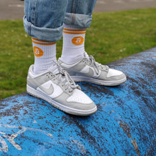 Lade das Bild in den Galerie-Viewer, Person trägt weiße Bitcoin Sportsocken mit orangen Streifen und Logo, kombiniert mit weißen Nike-Sneakers auf blauer Halfpipe